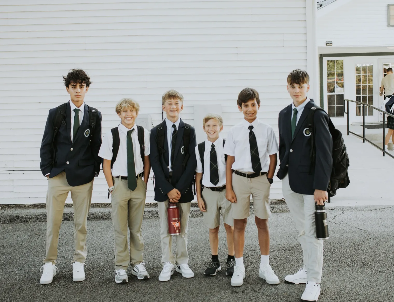 Students in school blazers and uniforms stand together outside their school