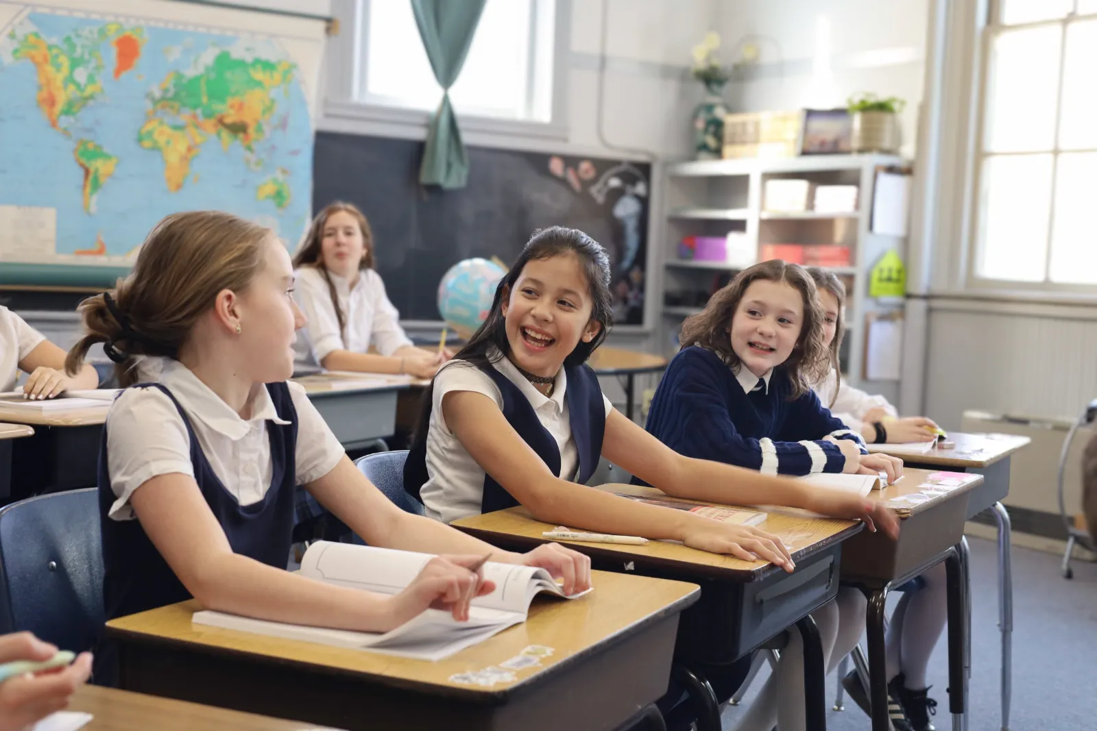 Students in uniform laugh together at their desks during class
