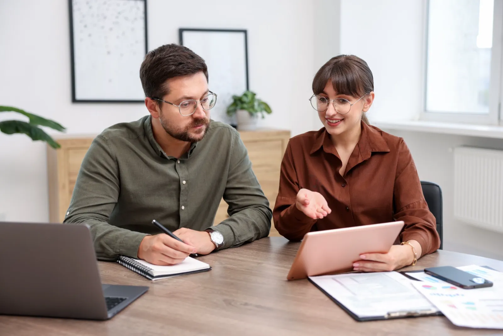 Two colleagues review plans together at a table with a laptop and tablet