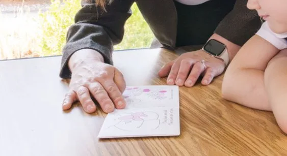 A teacher guides a student through a small book at a desk