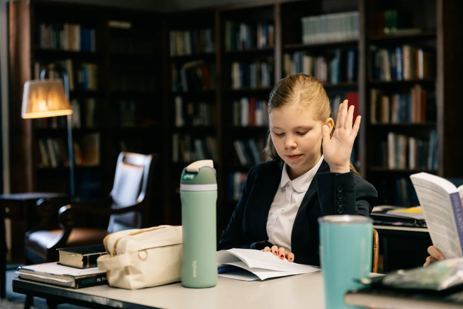 A student in a blazer raises a hand among library shelves