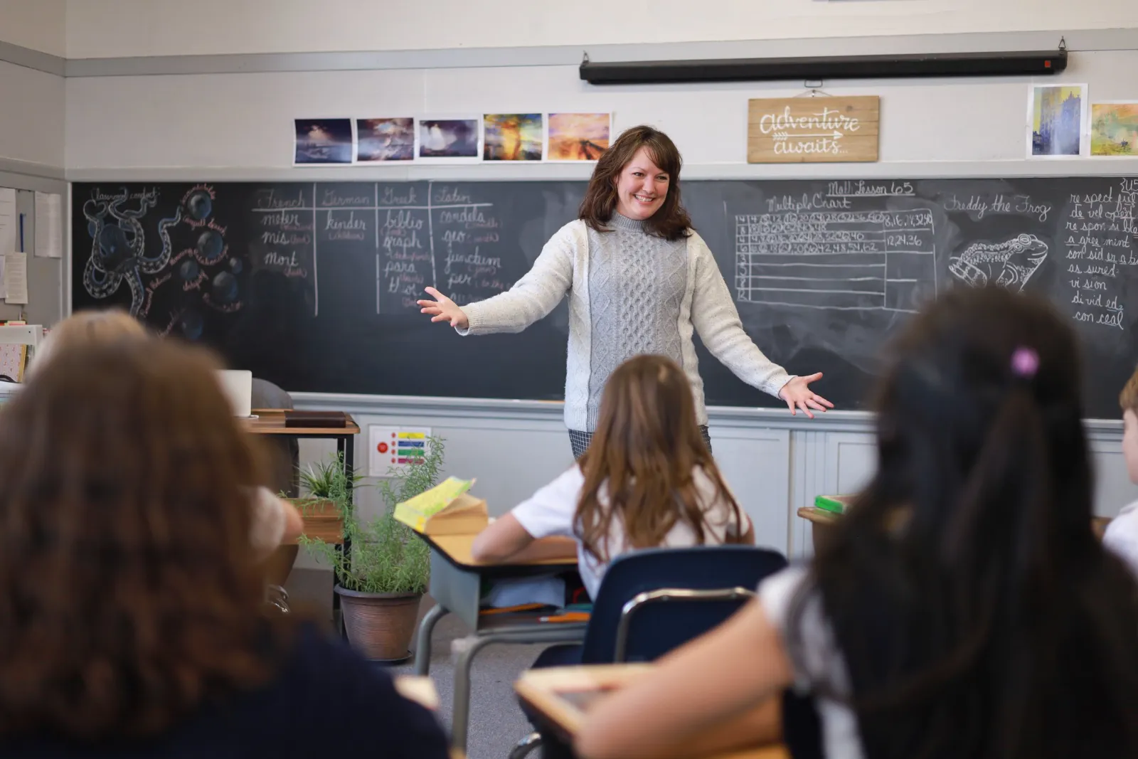 A teacher leads a lesson at the chalkboard as her students look on